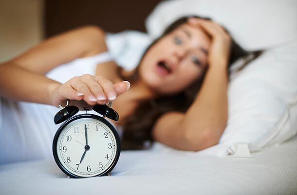 Frau im Bett macht den Wecker aus