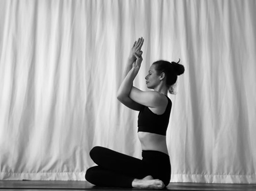 Frau sitzt auf dem Boden und hält die Yogapose Adlergesicht