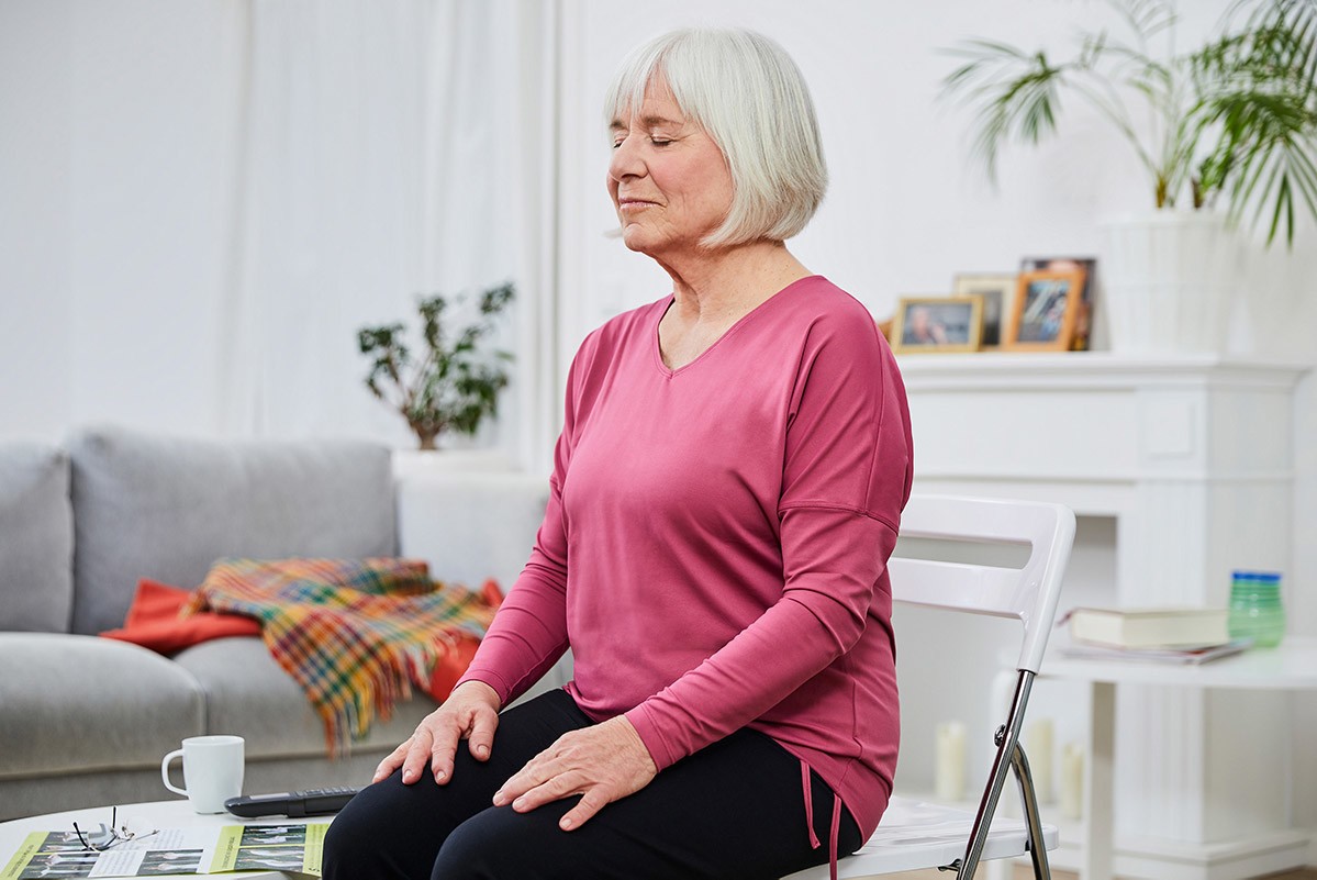 Yoga in jedem Alter Yoga in jedem Alter, eine aalte Dame sitzt auf einem Stuhl, hat die Augen geschlossen und macht Telefonyoga