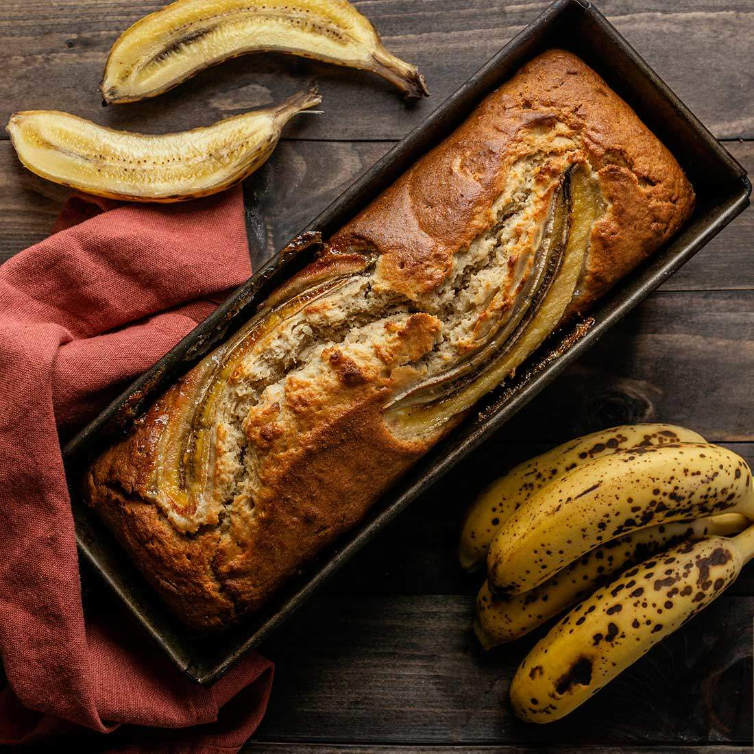 In einer Kuchenform ist ein Mandel-Kokos-Bananenbrot, daneben liegen reife Bananen als Ei-Alternative