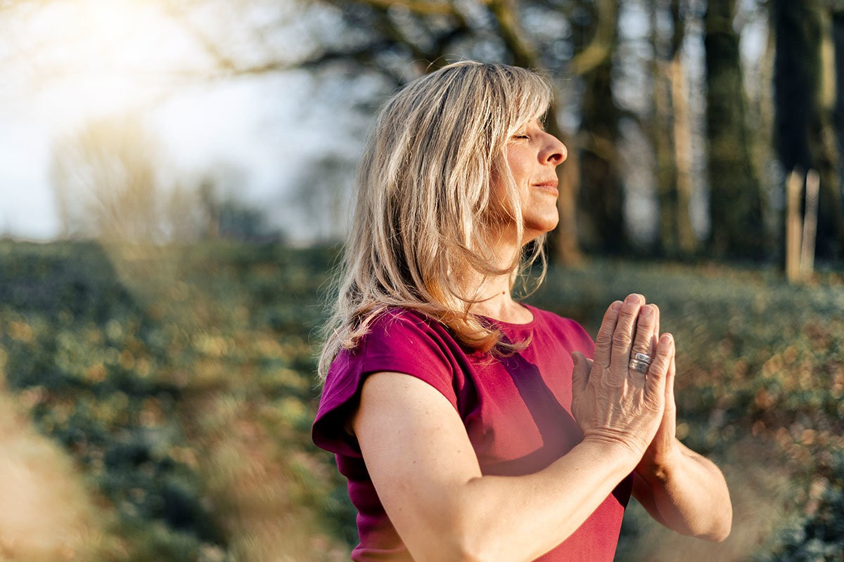 Yogini steht in der Natur und übt Achtsamkeitsmeditation aus