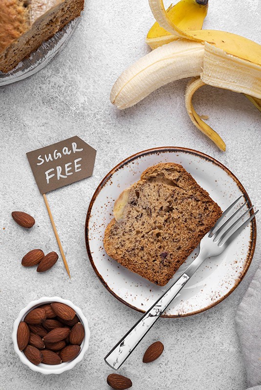 Mandel-Kokos-Bananenbrot geschnitten Das Mandel-Kokos-Bananenbrot wurde in Scheiben geschnitten, es ist Zuckerfrei, daneben liegt eine Banane und eine Schüssel mit Mandeln