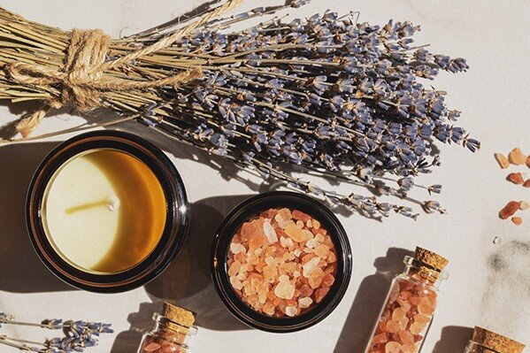 Lavendel Ein Bündel Lavendel, eine Kerze und Fläschchen gefüllt mit Salzen liegen auf einer weißen Unterlage