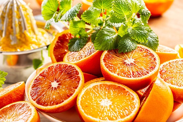 Orangenschalen mehrere halbierte Orangen liegen auf einem Brett, daneben ist ein Büschel Zitronenmelisse