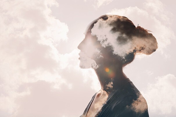 Yoga gegen Stress und Angst: Das Seitenprofil einer Frau ist zu sehen. Durch sie hindurch sind Wolken zu sehen.