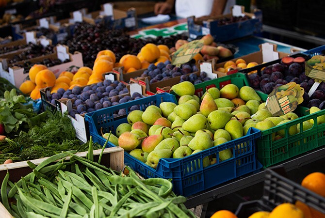 Kaufe saisonal und regional ein Bei einem Markstand stehen viele Kisten an Obst und Gemüse nebeneinander.