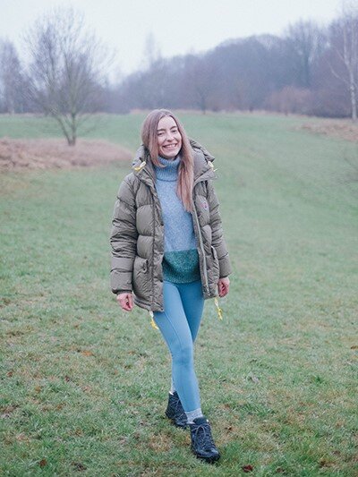 Frische Luft Ein Mädchen trägt die Leggings Shakti, einen Wollpilli und eine jacke. Sie steht auf einem nebeligen feld und lächelt in die Kamera