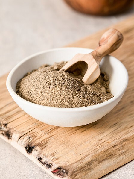 Maca In einer weißen Schüssel auf einem Holzbrett befindet sich Maca-Pulver
