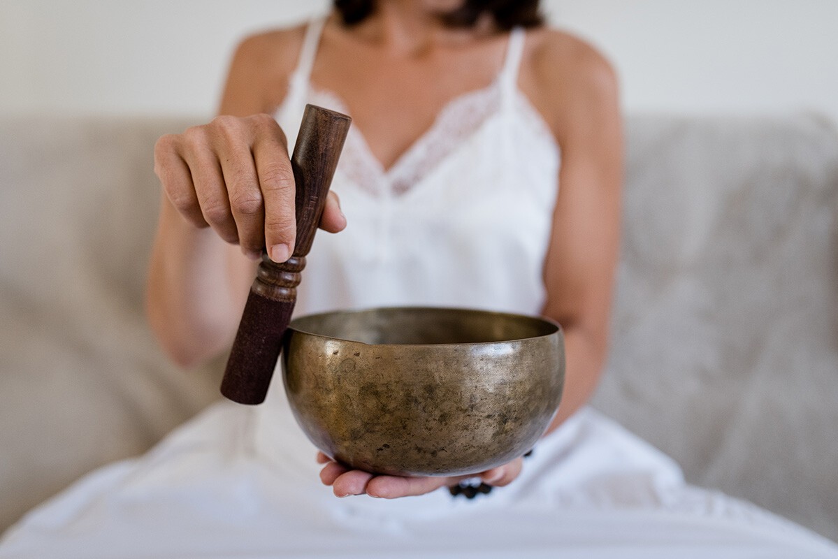 Klangmeditation Blogbild Eine Frau hält eine Klangschale und einen Klangstab für die Klangmeditation vor sich