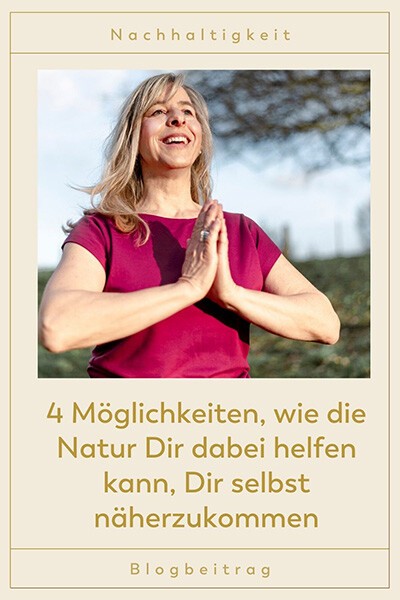 4 Möglichkeiten, wie die Natur Dir dabei helfen kann, Dir selbst näherzukommen Eine Frau hat ihr Hände vor der Brust gefaltet und steht in der Natur, sie lächelt glücklich