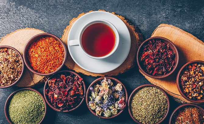 Ayurveda Auf mehrere Schüsseln sind verschiedene Kräuter verteilt auch eine Tasse Tee zum Fasten steht neben den Schüsseln