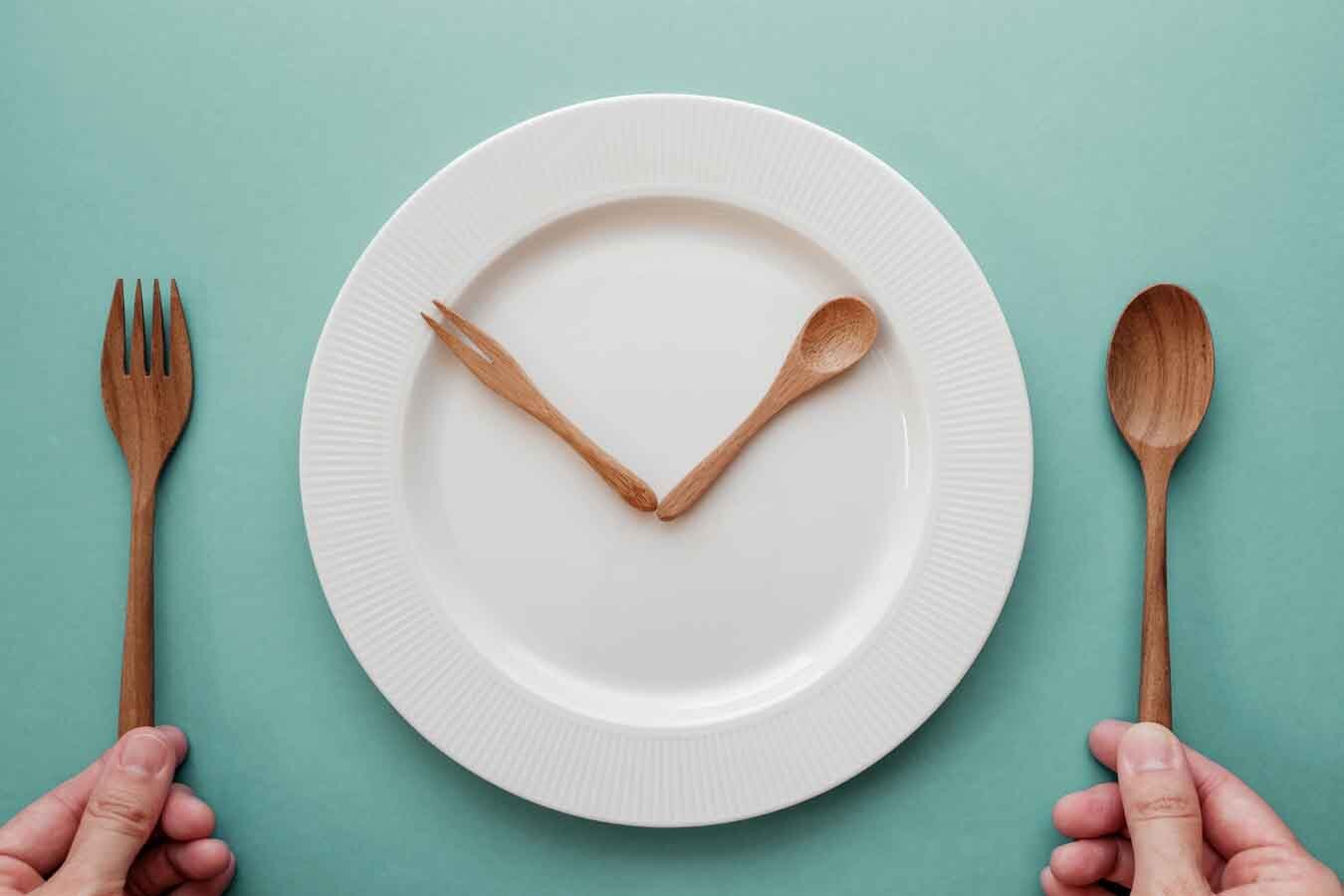 Intervall-Fasten, wooden spoon and fork as a clock hands on white plate, Intermittent fasting concept, ketogenic diet, weight loss, skip meal