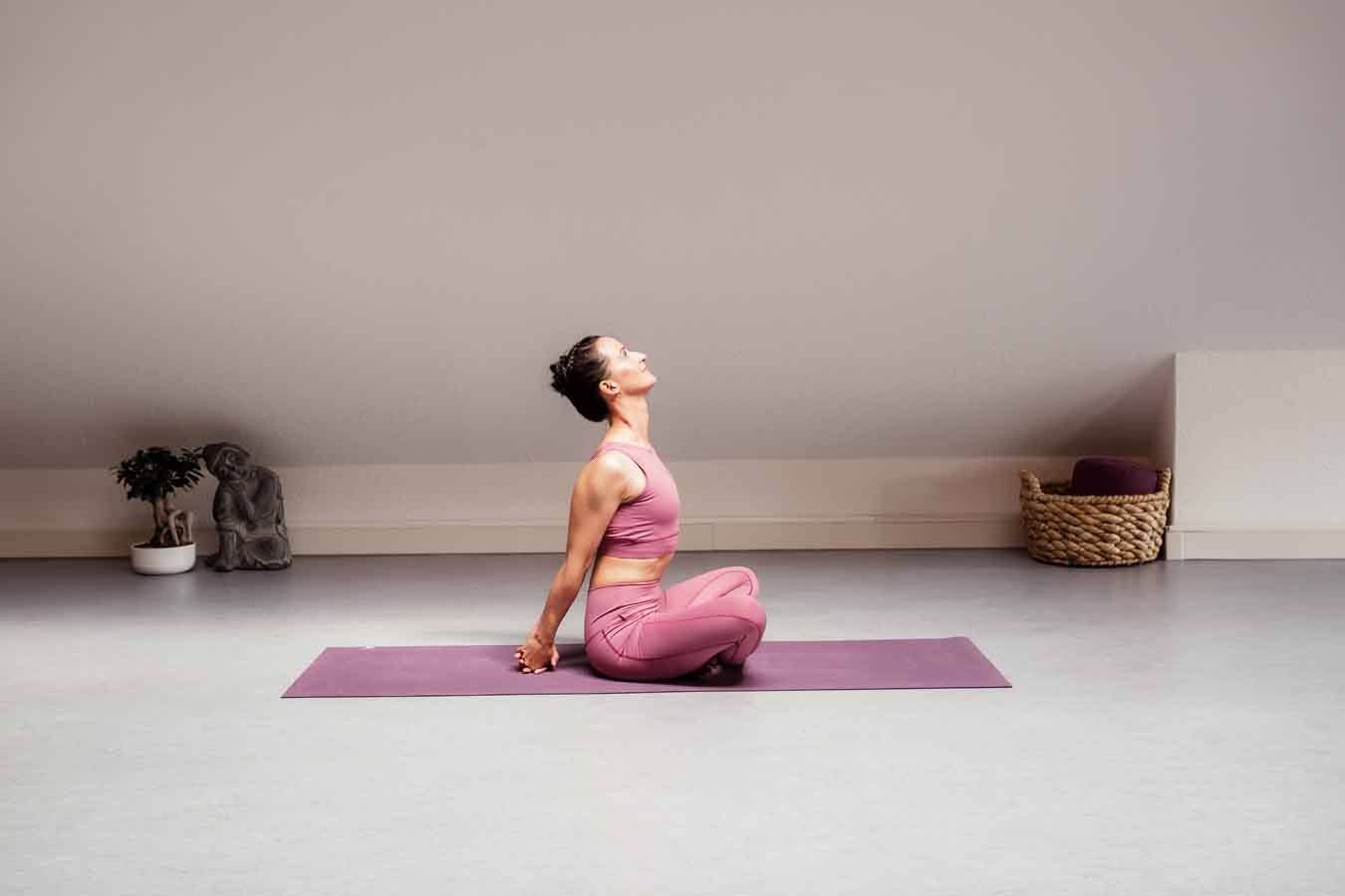 Frau sitzt im Schneidersitz auf einer Yogamatte in einem Yogastudio und macht Yoga für die Organe.