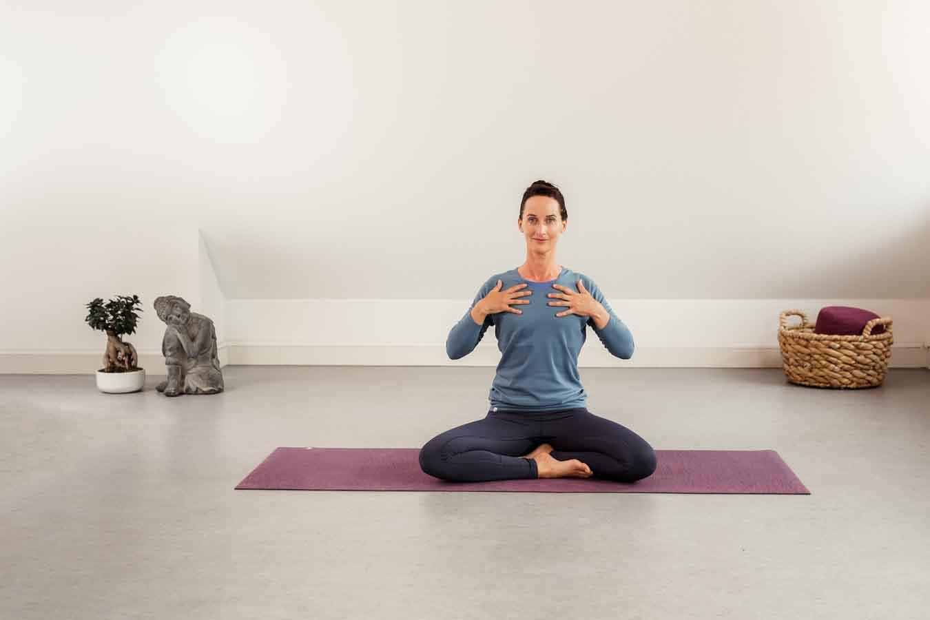 Frau sitzt im Schneidersitz auf einer Yogamatte in einem Yogastudio und macht Yoga für die Organe.